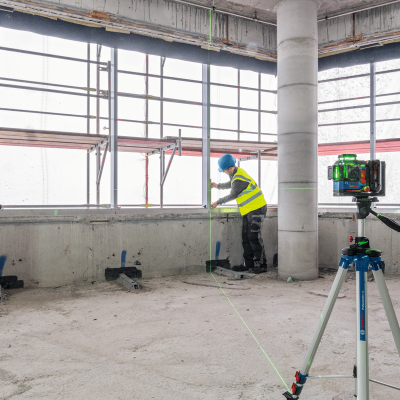 Tripé com instrumento de medição a laser Bosch e trabalhador de construção com colete amarelo e capacete azul
