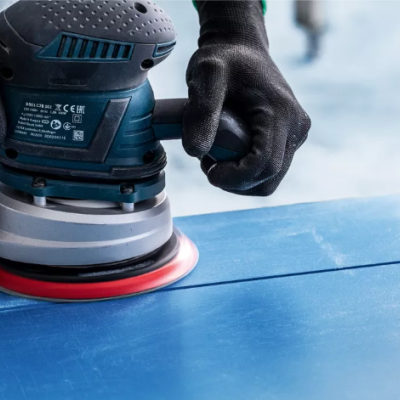 Lixadora elétrica azul a ser utilizada com luvas pretas numa superfície azul