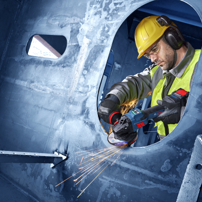 Trabalhador com esmerilhadora elétrica BOSCH corta metal azul num ambiente industrial