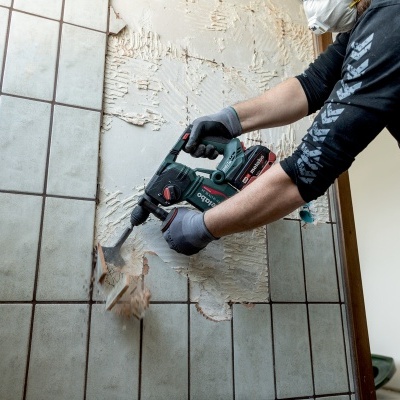 Pessoa a remover azulejos cinzentos de parede com ferramenta elétrica sem fio