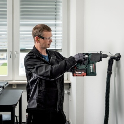 Homem com furadeira a trabalhar numa parede numa sala com janela e mesa.