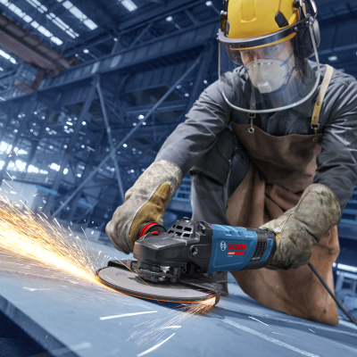 Trabalhador a usar rebarbadora Bosch para cortar metal com faíscas numa fábrica.