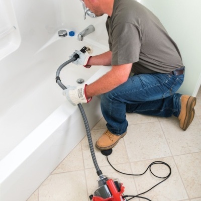 Homem a usar máquina elétrica vermelha para desentupir banheira branca em casa de banho clara