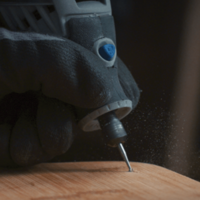 Rebolo rotativo cinza com botão azul a usar numa peça de madeira clara