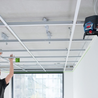 Homem ajusta estrutura metálica suspensa no teto em sala com janelas amplas
