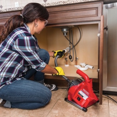 Mulher a desentupir cano de cozinha com ferramenta vermelha