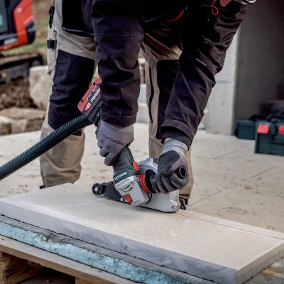 Pessoa a usar lixadeira elétrica em pedra sobre bancada de madeira num canteiro de obras