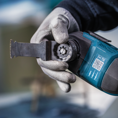 Ferramenta elétrica azul e preta com lâmina metálica serrilhada e mão com luva cinza a segurá-la