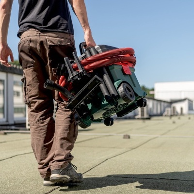 Homem com aspirador portátil verde com detalhes vermelhos no teto de um edifício