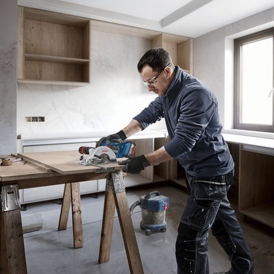 Homem a cortar madeira com máquina circular numa bancada interior