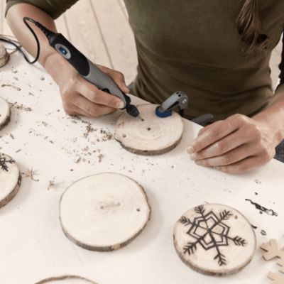 Pessoa a gravar desenhos em discos de madeira com ferramenta elétrica numa mesa com vários discos e fios de lã