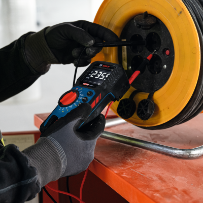 Multímetro digital Bosch medindo corrente numa bobina de extensão elétrica amarela e preta.