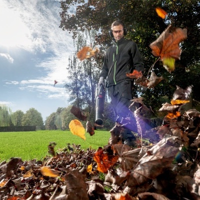 Pessoa com soprador de folhas a limpar folhas secas num relvado