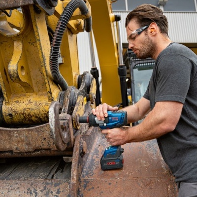 Homem a usar aparafusadora elétrica numa máquina pesada amarela num ambiente industrial