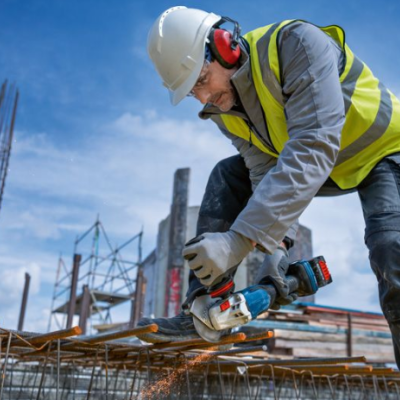 Trabalhador de construção a cortar barras de metal com rebarbadora num estaleiro