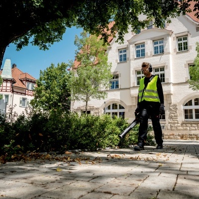 Pessoa com colete refletor e soprador de folhas numa calçada de pedra