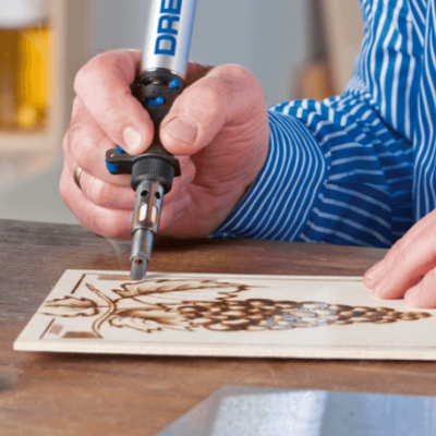 Pessoa gravando padrão de uvas em madeira com ferramenta DREMEL na mesa