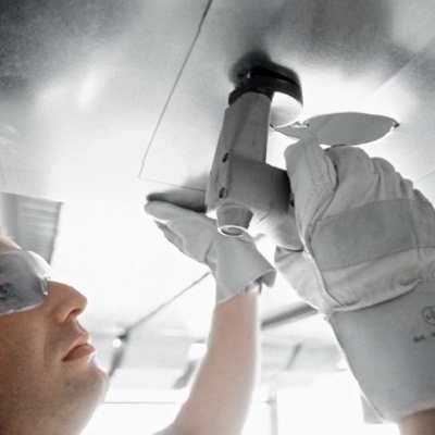 Pessoa a usar óculos de proteção e luvas a trabalhar com ferramenta elétrica no teto metálico