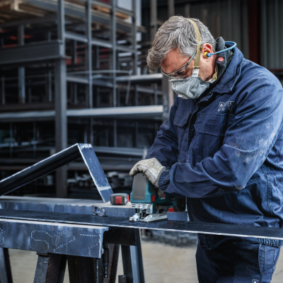 Homem a trabalhar com uma ferramenta elétrica num objeto metálico preto em ambiente industrial