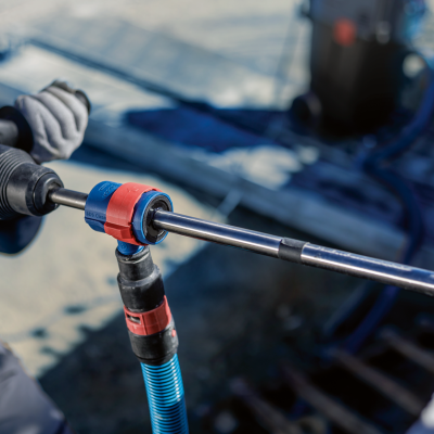 Ferramenta elétrica azul com detalhes vermelhos e pretos em uso com tubo azul num ambiente industrial