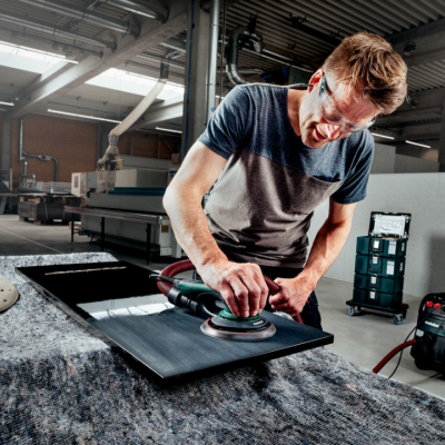 Homem a polir superfície preta com máquina elétrica em fábrica