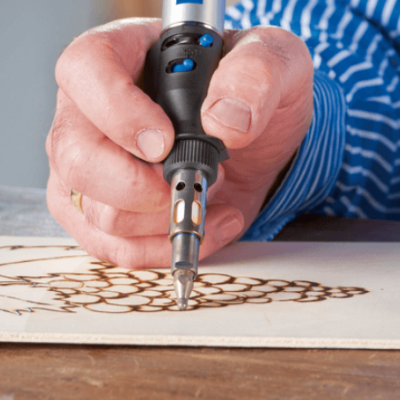 Mão a usar ferro de pirogravura para queimar desenho de uvas em madeira
