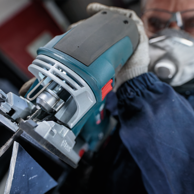 Serra tico-tico eléctrica azul e preta em uso cortando metal por pessoa com proteção