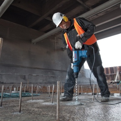 Trabalhador da construção usando martelete elétrico azul em chão de concreto