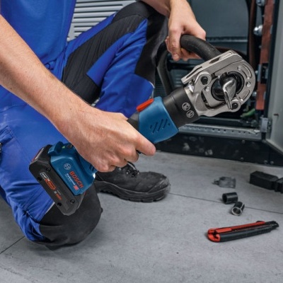 Ferramenta elétrica Bosch com bateria preta e azul em uso por pessoa com roupa azul, chão cinzento de oficina