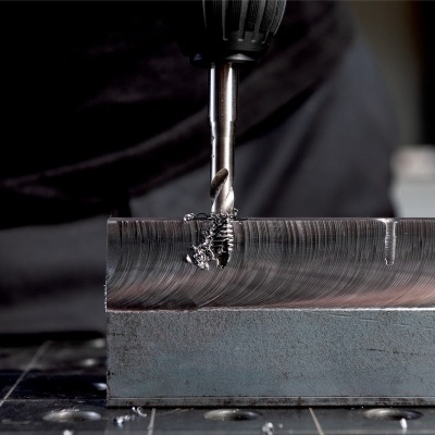 Broca metálica perfurando peça de metal prateada com limalhas