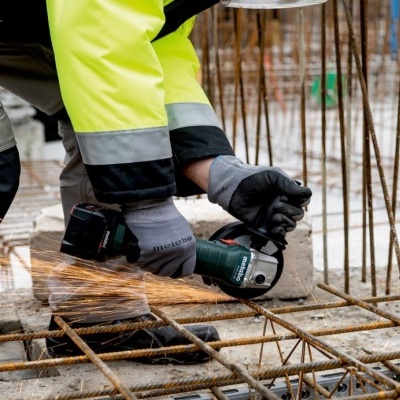 Pessoa a cortar estrutura de ferro com rebarbadora elétrica em obra