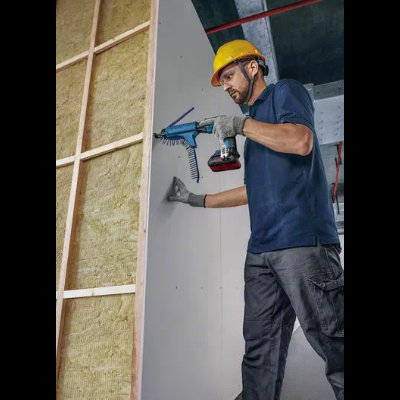 Homem com capacete amarelo a instalar painel de gesso branco numa estrutura de madeira com isolamento.