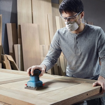 Homem a lixar porta de madeira com lixadora elétrica numa oficina