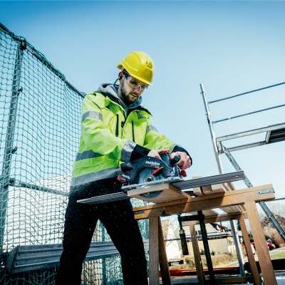 Homem com capacete e colete de segurança a cortar madeira com serra circular
