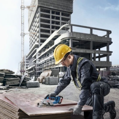 Trabalhador da construção a cortar placa de madeira com serra elétrica no estaleiro