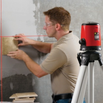Laser de nivelamento vermelho em tripé e homem a medir azulejo à parede