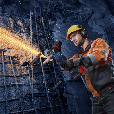 Homem a cortar barras metálicas com esmeriladora numa parede de cimento