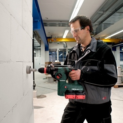 Homem a usar furadeira sem fios numa parede branca em oficina