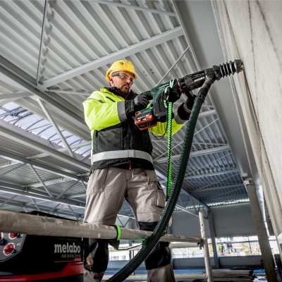 Homem com capacete e jaqueta amarela usando ferramenta elétrica Metabo numa parede de concreto