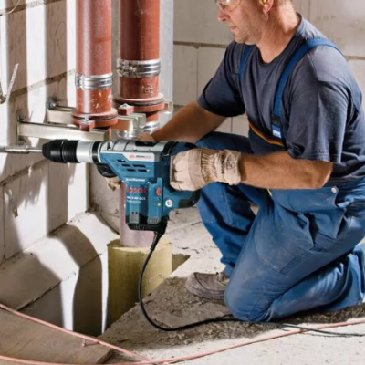 Homem com macacão azul a usar furadeira elétrica azul em canteiro de obras