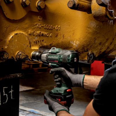 Pessoa usando ferramenta elétrica Metabo verde para apertar parafusos numa peça industrial amarela.