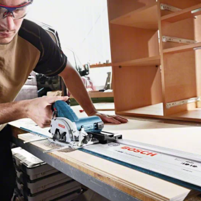 Pessoa com serra circular BOSCH cortando madeira clara em oficina