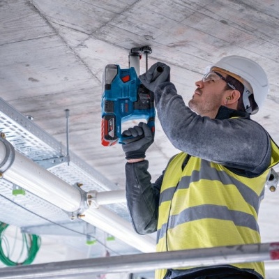 Trabalhador da construção civil com colete amarelo perfurando teto de betão com furadeira azul