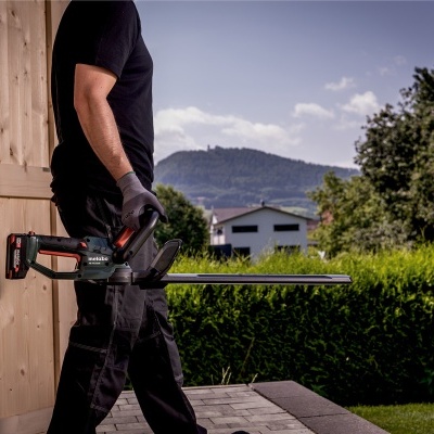 Pessoa segurando aparadora de sebes elétrica em jardim