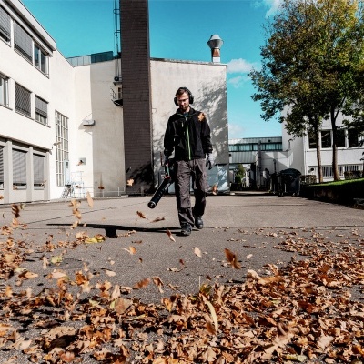 Homem com soprador de folhas elétrico em área externa com folhas secas no chão