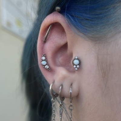Orelha com múltiplos piercings de prata e cabelo azul