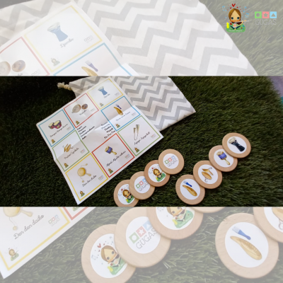 Fichas redondas em madeira com imagens coloridas e cartão de jogo sobre relva artificial, junto a saco tecido cinzento e branco