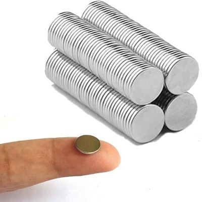 Ímanes redondos prateados empilhados e um íman na ponta de um dedo