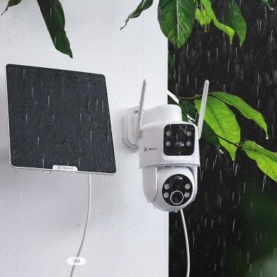 Câmara de vigilância branca com antenas e placa solar preta montadas numa parede branca sob chuva