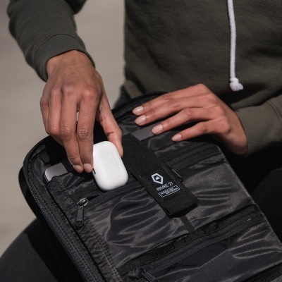 Mochila ou pasta preta aberta com vários compartimentos, mãos a guardar estojo branco para auscultadores